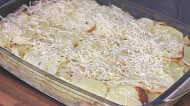 Kadın patatesli bir tabağa rendelenmiş peynir koyar. Evde yemek pişirmek..
