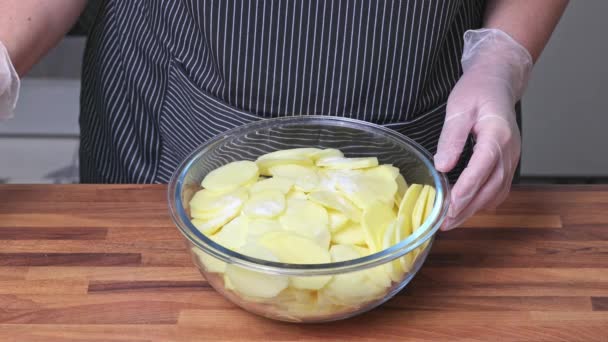 女性はスパイスとクリームをガラスプレートに薄くスライスしたジャガイモに加えます 自宅で料理する — ストック動画