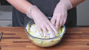 Bir kadın baharatla kremayı ince dilimlenmiş patatesle cam tabakta karıştırır. Evde yemek pişirmek..