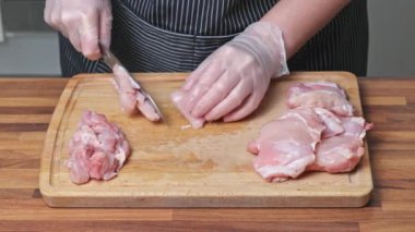 Tahta kesme tahtasıyla taze tavuk etini çelik bıçakla doğrayan bir kadın. Evde yemek pişirmek..