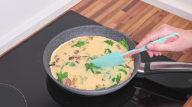 Mantarlı yumurta, pastırma ve tavada ıspanak kızartan bir kadın.