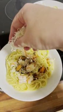 Kadın deniz ürünleriyle spagetti pişiriyor. Dişi el spagettiye rendelenmiş peynir serpiyor..