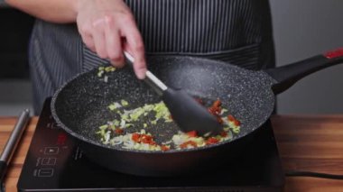 Bir kadın kızartma tavasında soğan ve kurutulmuş domates kızartıyor.