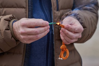 Erkek elinin fitille havai fişek ateşlemesine yaklaş. Elinde yanan bir patlayıcıyı tutan adam.