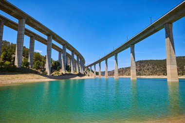 Explore the tranquil scene under the bridge Viaducto de Contreras through reservoir. clipart