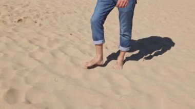 Kumsalda kumsalda yürüyen ayaklar, yakın plan. Sıcak kumda yalın ayak yürüyen bir adam. Seyahat, macera.