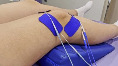 Diz için fizyoterapi. Dizinde elektro uyarıcı elektrotlar olan insan bacağı..
