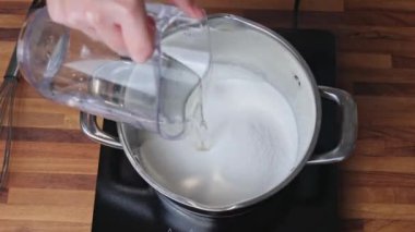 Ev mutfağındaki bir tencerede mandalina reçeli pişirmek için şeker şurubu hazırlıyorum.