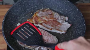 Bir kadın tavada iki parça et kızartır.