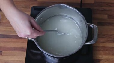 Ev mutfağındaki bir tencerede mandalina reçeli pişirmek için şeker şurubu hazırlıyorum.