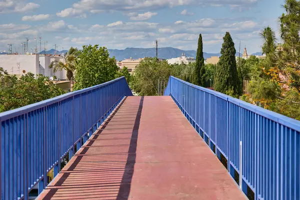 Mavi korkuluklu ve mavi gökyüzünün altında Valencia 'da şehir manzaralı kırmızı yaya köprüsü.