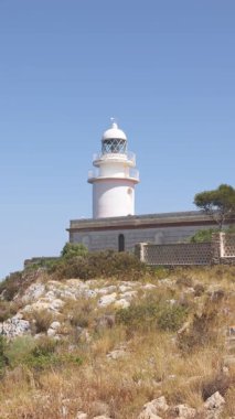 İspanya, Xabia yakınlarındaki Cape Sant Antoni 'deki beyaz deniz fenerinin manzarası, açık mavi gökyüzünün altında Akdeniz' in üzerindeki bir uçurumun üzerinde duruyor.