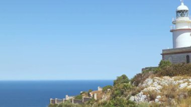 İspanya, Xabia yakınlarındaki Cape Sant Antoni 'deki beyaz deniz fenerinin manzarası, açık mavi gökyüzünün altında Akdeniz' in üzerindeki bir uçurumun üzerinde duruyor.