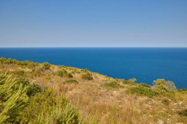 İspanya 'nın Javea kentindeki Cape Sant Antoni' deki kayalıklardan Akdeniz manzarası açık mavi su ve gökyüzü ufka kadar uzanıyor.