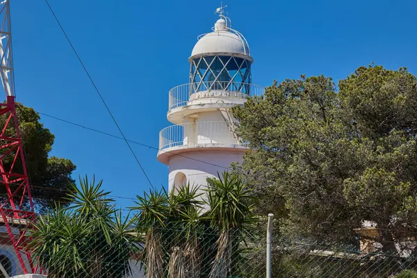 İspanya, Xabia yakınlarındaki Cape Sant Antoni 'deki beyaz deniz fenerinin manzarası, açık mavi gökyüzünün altında Akdeniz' in üzerindeki bir uçurumun üzerinde duruyor.
