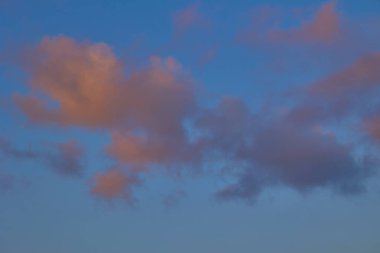 Gün batımında mavi gökyüzünde renkli akşam bulutları, ılık ışıkla yumuşak doğal arka plan.