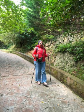 Yürüyüş direkleri olan bir dişi turist yolda yürüyor..