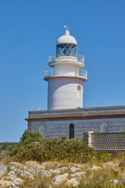İspanya, Xabia yakınlarındaki Cape Sant Antoni 'deki beyaz deniz fenerinin manzarası, açık mavi gökyüzünün altında Akdeniz' in üzerindeki bir uçurumun üzerinde duruyor.