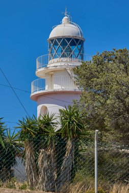 İspanya, Xabia yakınlarındaki Cape Sant Antoni 'deki beyaz deniz fenerinin manzarası, açık mavi gökyüzünün altında Akdeniz' in üzerindeki bir uçurumun üzerinde duruyor.