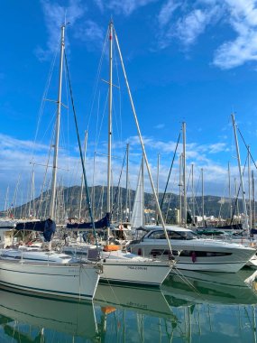 Mavi gökyüzü ve bulutların altında yatları ve dağları olan Denia marinası. Denia, İspanya - 24 Mayıs 2025.