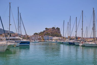 Denia marinasında arka planda tarihi Denia Kalesi 'nin yükseldiği yatların manzarası. Denia, İspanya - 31 Mayıs 2025.