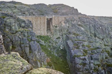 Kayalık dağ manzarasında eski bir taş köprü.