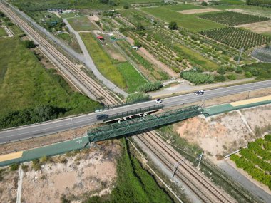Tarım arazisiyle çevrili bir demiryolu üzerindeki bir yol köprüsünün insansız hava aracı görüntüsü.