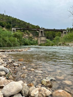 Nehrin üzerinde kayalık kıyı ve yeşil bitki örtüsüyle eski taş köprü..