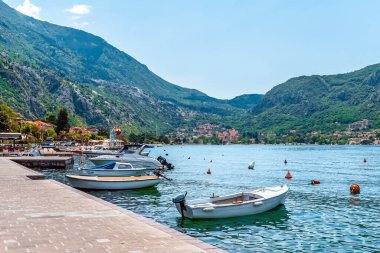 Dobrota rıhtımına yanaşmış küçük teknelerin huzurlu bir manzarası. Körfezin berrak suları ve çevreleyen yeşil tepeler, dağlarda yuva yapmış uzak evleri olan sakin bir atmosfer yaratıyor. Kotor, Karadağ - 18 Haziran 2021