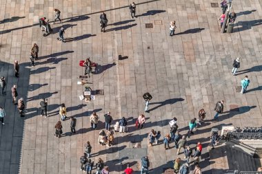 Yürüyen insanların hava görüntüsü ve Madrid şehir meydanında gösteri yapan bir sokak müzisyeni, gün ortası güneşinde uzun gölgeler bırakıyor. Hareketli şehir manzarası İspanyol başkentinin canlı atmosferini yakalar. Madrid, İspanya - 30 Kasım 2021