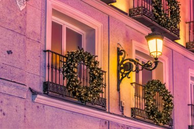 A beautifully decorated balcony with festive Christmas wreaths and warm lights in Madrid during the 2021 holiday season, Spain. The glowing streetlamp adds to the cozy ambiance of the evening clipart