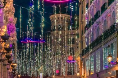 Madrid 'in aydınlık caddesi, İspanya 2021 şenlik sezonunda Noel ışıkları ve parlak neon halkalar ile parıldıyor. Karmaşık bina detayları ve asılı ışıklar büyülü bir tatil atmosferi yaratır.