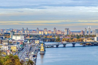 Bir sonbahar günü Kyiv 'in şehir silueti ve Dnipro Nehri' nin panoramik manzarası, kentin modern ve klasik mimarisi Ukrayna 'nın karışımını gözler önüne seriyor. Manzarada köprüler, yüksek binalar ve nehir kıyıları boyunca renkli yapraklar ön plana çıkıyor.