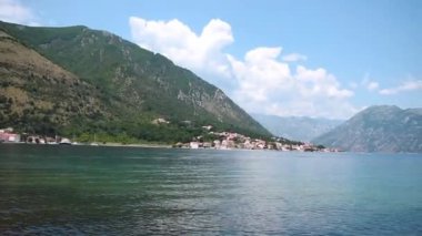 Karadağ 'ın Kotor kenti yakınlarındaki Dobrota köyünden Kotor Körfezi' nin nefes kesici panoramik manzarası. Video 11 saniye. Sakin sular çarpıcı dağları ve canlı bir yaz gökyüzünün altındaki güzel kıyı kasabasını yansıtıyor.