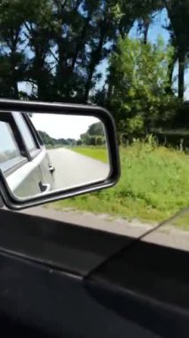 Hızlı giden araba Ukrayna 'nın Sumy bölgesindeki bereketli bir yaz ormanından geçiyor. Dikey 4k video, 52 saniye. Dikiz aynası asfalt bir yol ve canlı bir yeşillik yansıtır, dinamik ve sürükleyici bir perspektif yaratır.