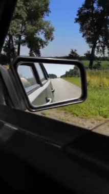 Yeşilliklerin arasından geçen verimli bir yaz yolculuğunun çift perspektifi: Yolcu penceresinden geçen ağaçlar ve doğa ve yan aynaya yansıyan asfalt bir yol. Dikey 4k video, 24 saniye. Orman arazilerinde huzurlu bir yolculuk