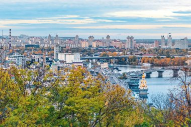 Ukrayna 'nın başkenti Kyiv' in panoramik bir görüntüsü, şehrin çeşitli mimarisi ve Dinyeper Nehri ile manzarasını gözler önüne seriyor. Sonbahar renkleri şehir manzarasına canlı bir dokunuş ekler.