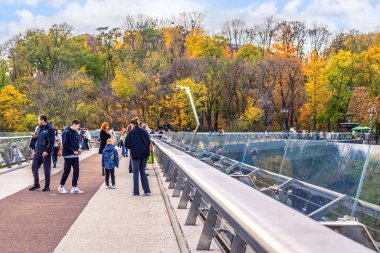 Kyiv, Ukrayna - 27 Ekim 2023: Kyiv 'in Cam Köprüsü' nde insanların sonbahar yaprakları arasında gezintinin keyfini çıkardıkları canlı bir sahne. Köprünün şeffaf tasarımı çevredeki manzaranın manzaralı görünmesini sağlar.