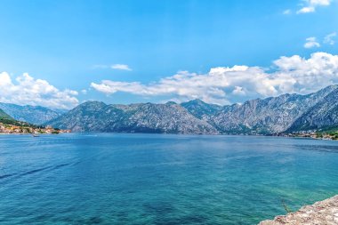 Karadağ 'ın Kotor Körfezi manzaralı ve arka planda sakin mavi sular ve görkemli dağlar var. Berrak gökyüzü ve güzel kıyı köyleriyle huzurlu bir yaz günü.