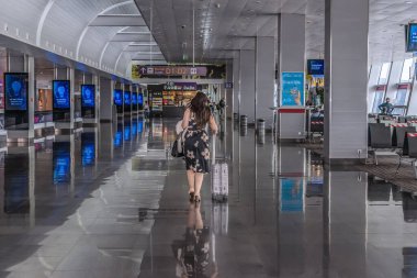 Kyiv, Ukraine - June 16, 2021: A woman with a suitcase walks along the corridor in the departure area at Boryspil International Airport in Kyiv - view from the back. Modern interior of Terminal D clipart