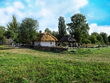 Ukraine, Pyrohiv (Kyiv) - September 17, 2017: Landscape of the Ukrainian traditional village. A clear sunny day, a wicker fence, a white hut with a thatched roof and a few beehives in the courtyard clipart