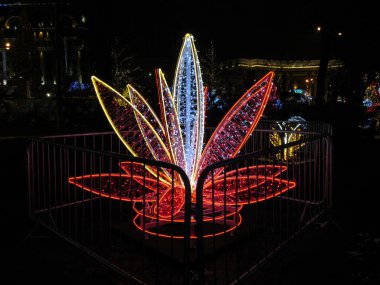 Kyiv, Ukraine - December 31, 2017: Beautiful festive magic sculpture in the form of a red lily flower at the Festival of Illuminations NeoYear 2018 on Sofia in Kyiv. A large flower from neon lights grows in a fairy garden at night among the other lig clipart