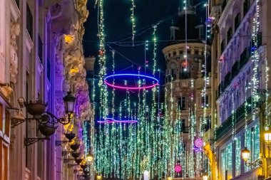 İspanya 'nın 2021 yılının şenlik sezonunda Madrid' de bir caddeyi aydınlatan Noel ışıkları. Parlak ışıklar, neon halkalar ve asılan ampuller de dahil olmak üzere, arka planda güzel mimari detaylarla büyülü bir tatil atmosferi yaratır.