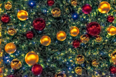 Parlak parıldayan ışıklarla aydınlatılan parlak kırmızı ve altın süslemeli güzel dekore edilmiş bir Noel ağacının yakın plan görüntüsü. Şenlikli dekorasyonlar sıcak bir tatil ortamı yaratıyor ve mevsimin neşesini vurguluyor.