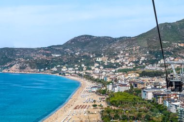 Türkiye 'nin Alanya kentindeki Kleopatra Sahili' nin panoramik manzarasında uzun ve kumlu bir kıyı şeridi, berrak Akdeniz suları ve çevreleyen dağlar yer alıyor. Sahildeki şehir doğa ve kentsel gelişimi birleştiriyor.