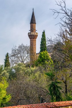 The minaret of the Suleymaniye Mosque rises above the greenery within Alanya Castle, Turkey. The historic mosque is a prominent feature of the landscape, framed by trees and traditional architecture clipart