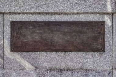 Gri granit duvarda kahverengi bronz bir plaka var. Köşelerinde dört yuvarlak cıvatalı eski paslı metal plakanın fotokopi arkaplanı