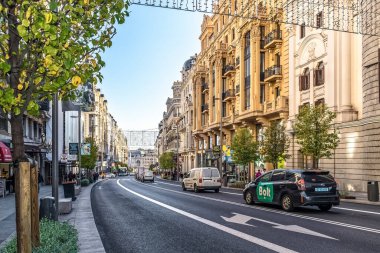Madrid, İspanya - 30 Kasım 2021: Madrid 'deki Gran Via' da Bolt taksi ve çeşitli araçların bulunduğu hareketli bir trafik manzarası şık binaların arka planına karşı. Sokaklar ağaçlarla ve dekoratif ışıklarla dolu.