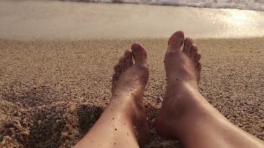 Türkiye 'nin Alanya kentindeki Kleopatra Sahili' nde dinlenen dişi bacaklar batan güneşin altın ışığıyla yıkandı. 4K video 17 saniye. Yumuşak deniz dalgaları sahili yıkıyor. Birinci şahıs perspektifi huzurlu bir plaj anını yakalar.