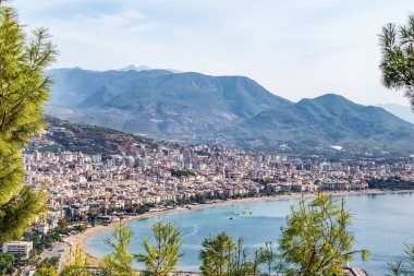 Türkiye 'nin Alanya kentinin manzarası, arka planda dağlar ve önde Akdeniz kıyı şeridi. Şehir körfez boyunca uzanır, çarpıcı bir doğal ve şehir manzarası sunar.